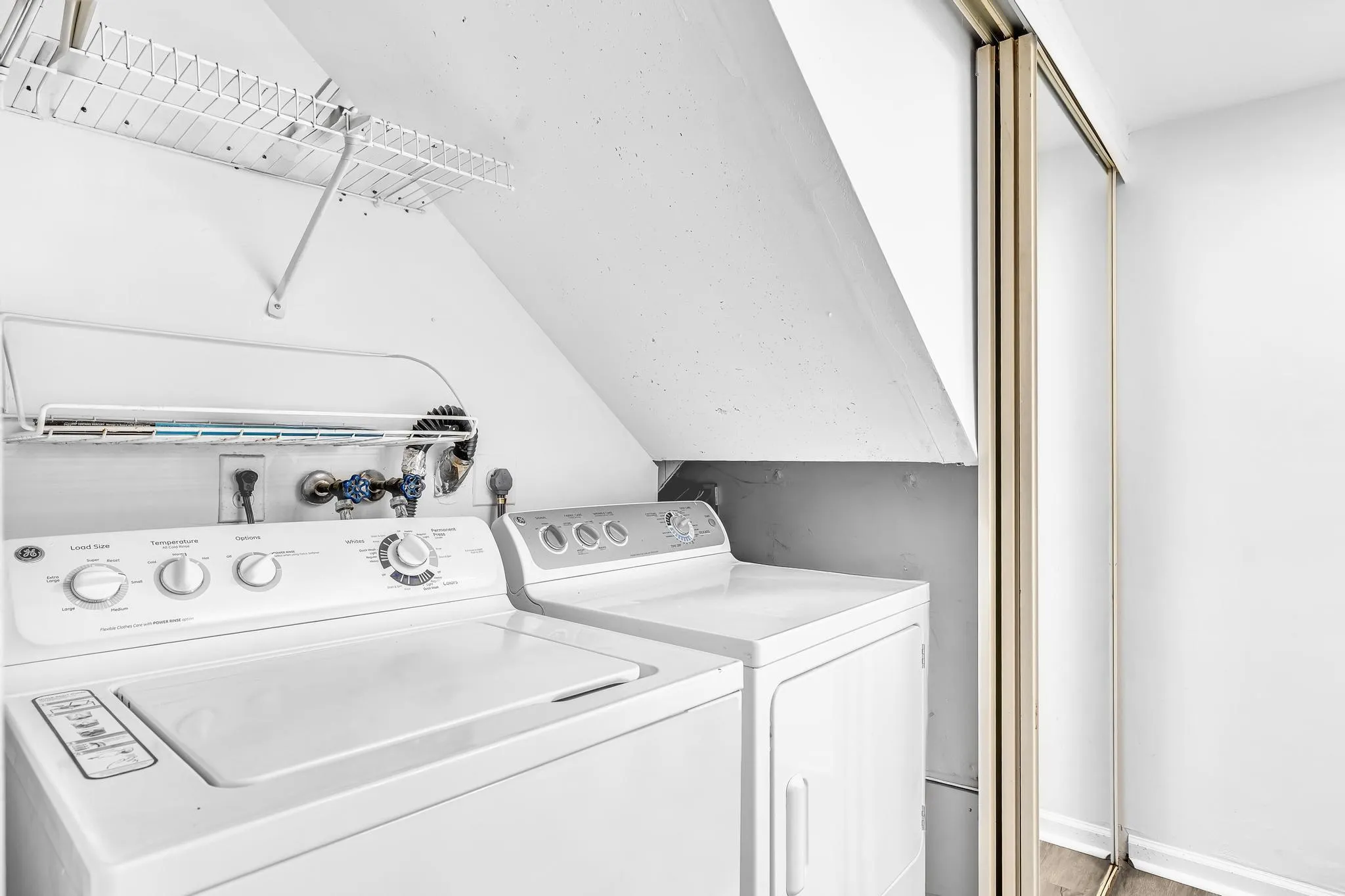 Dedicated laundry area featuring a top-load washing machine, front-load dryer, and wall-mounted wire shelving