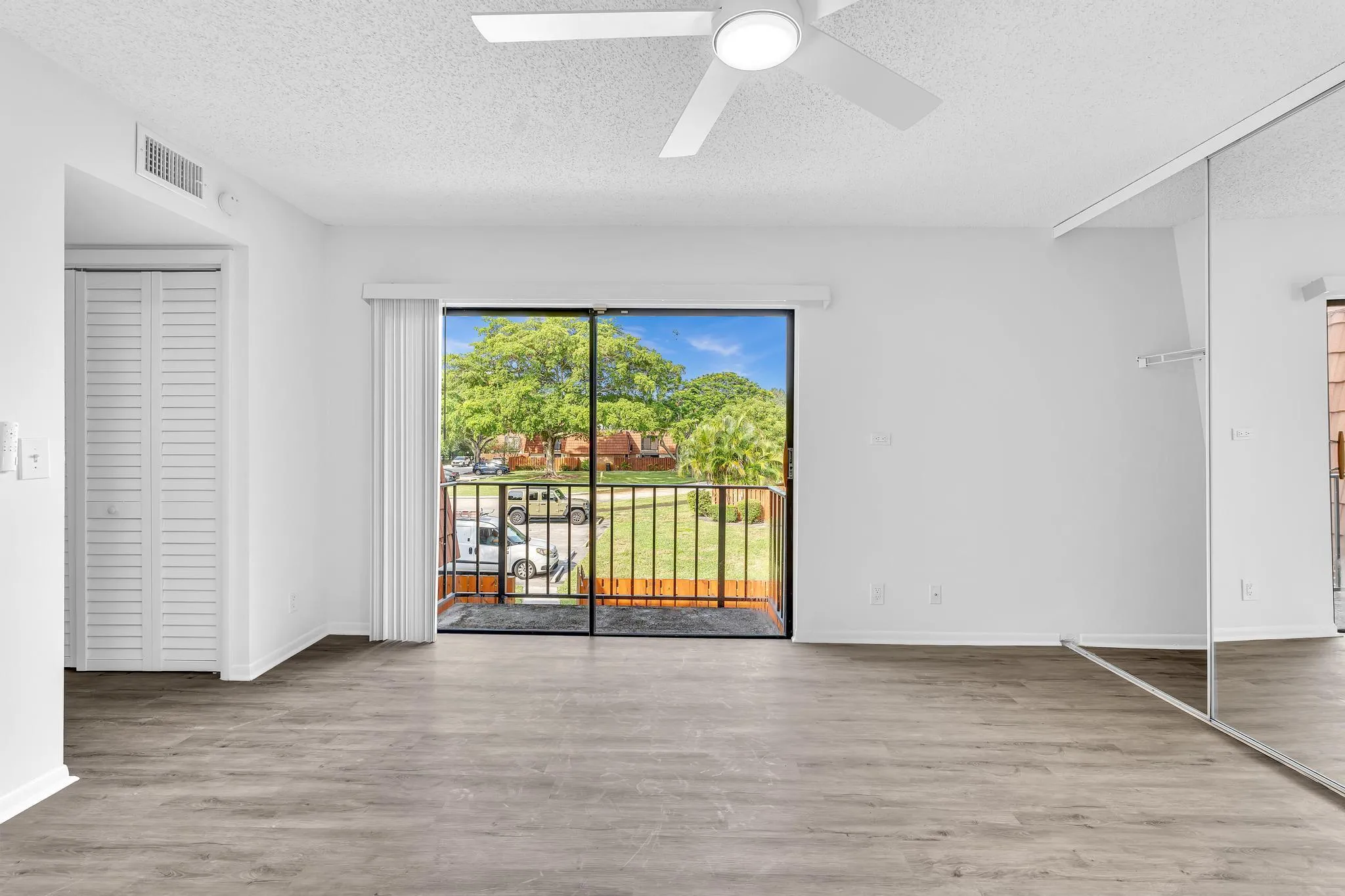 Open room featuring wood-finish flooring, a ceiling fan with integrated lighting, mirrored closet doors, and a sliding glass door to a private balcony