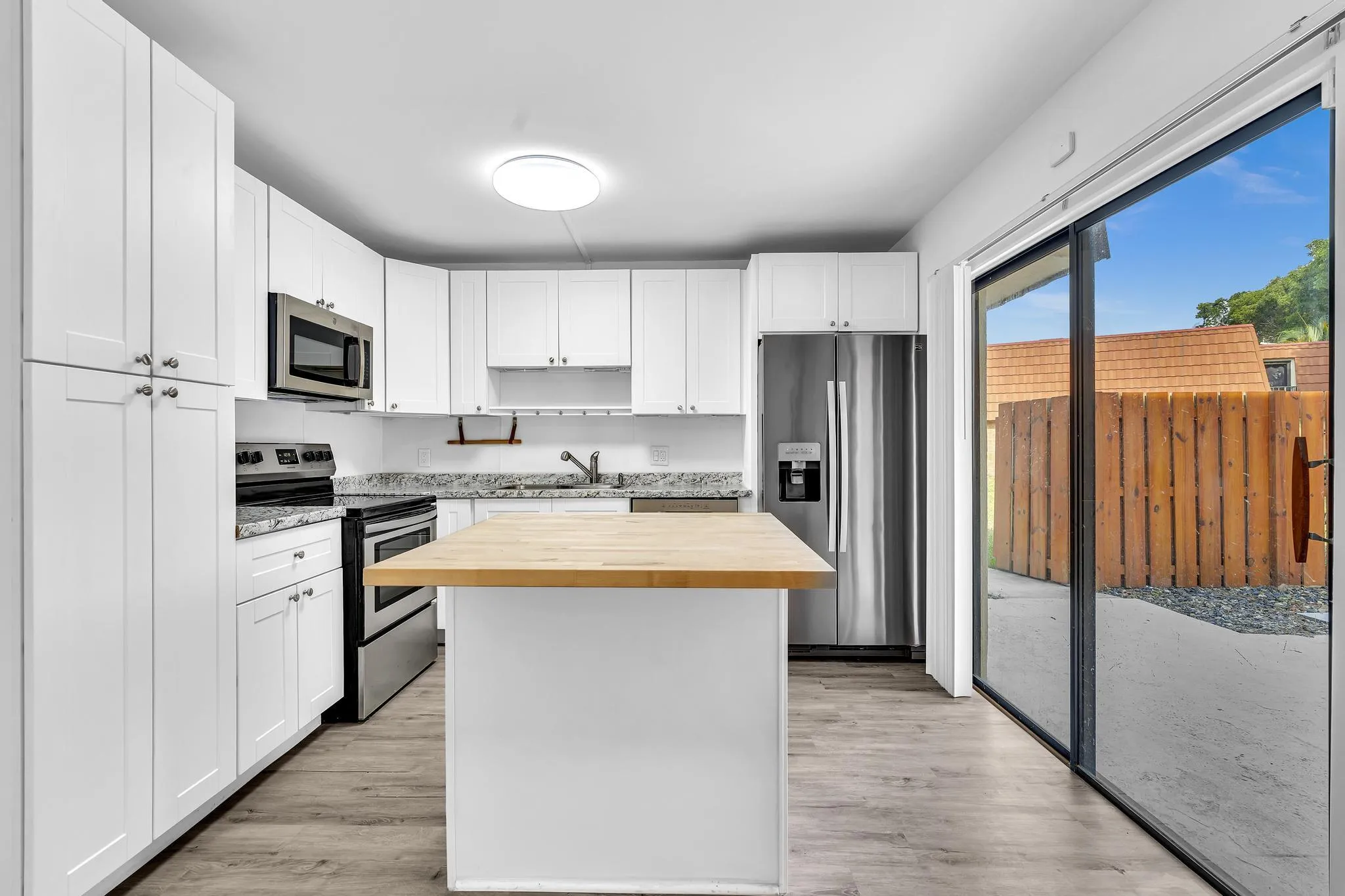 Modern kitchen featuring white shaker cabinetry, stainless steel appliances, light granite countertops, a butcher block island, and wood-finish flooring