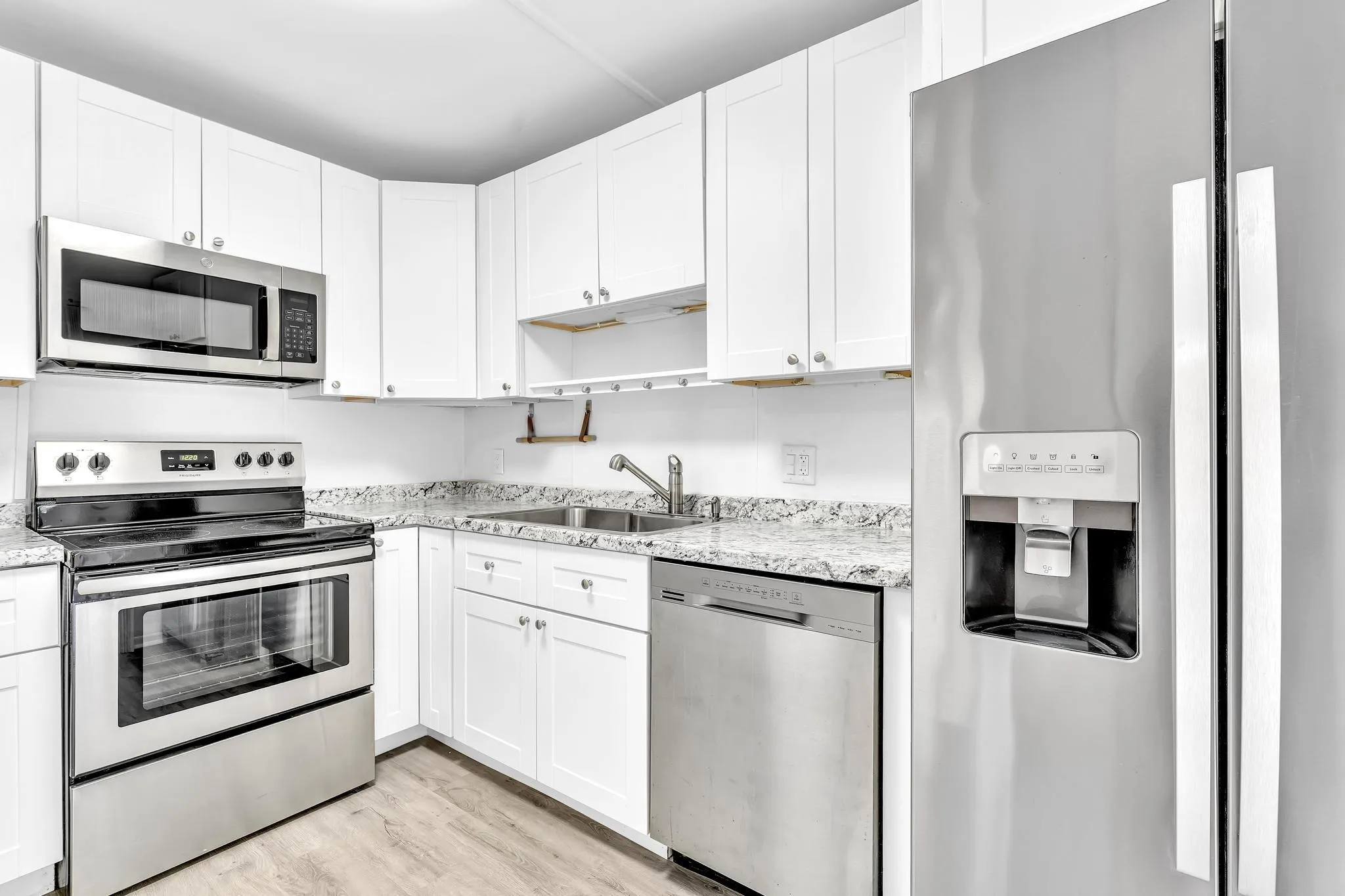 Kitchen featuring white cabinetry, stainless steel appliances, speckled countertops, and wood-finish flooring