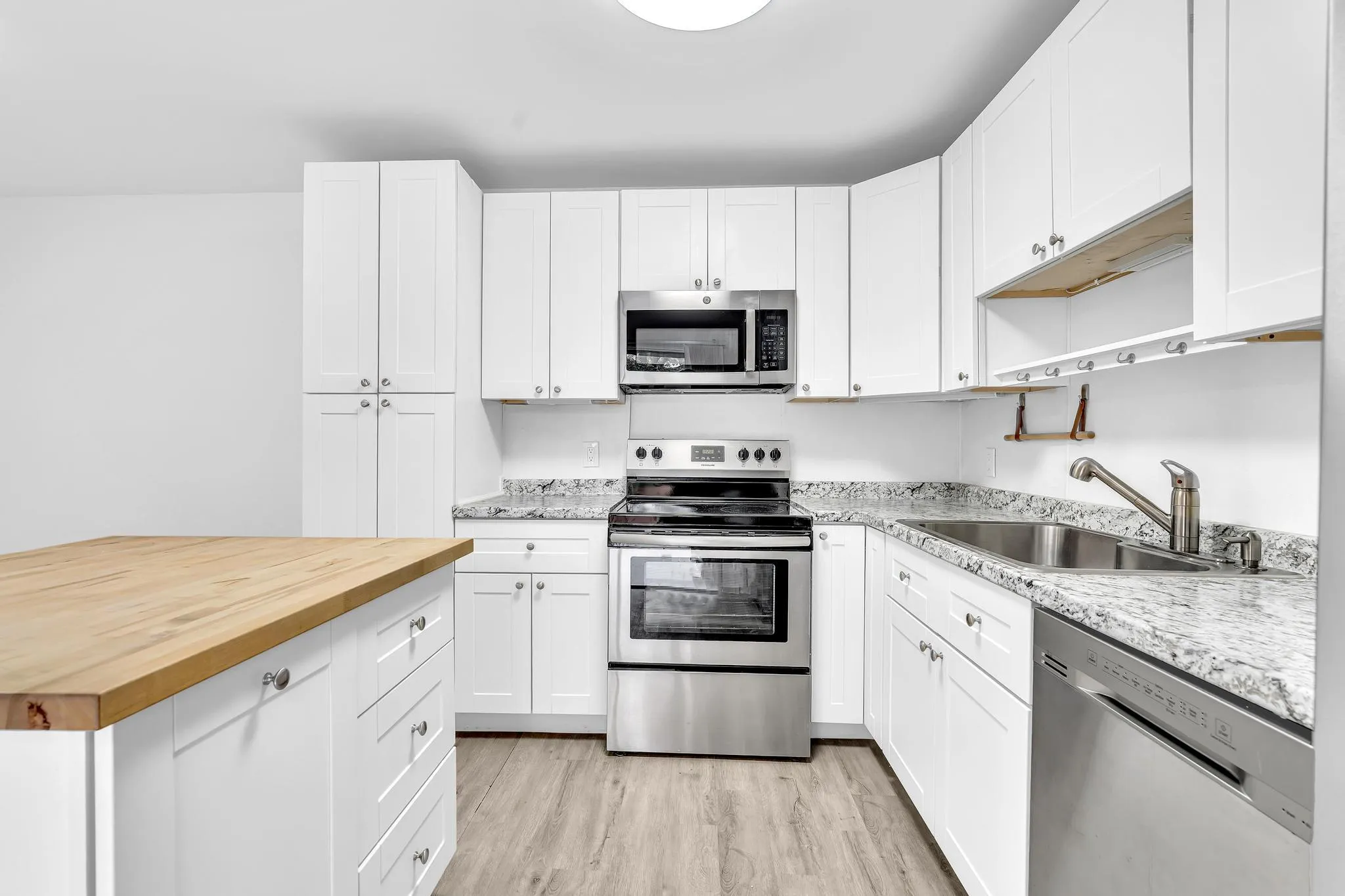 Kitchen featuring white cabinetry, stainless steel appliances, speckled countertops, and wood-finish flooring