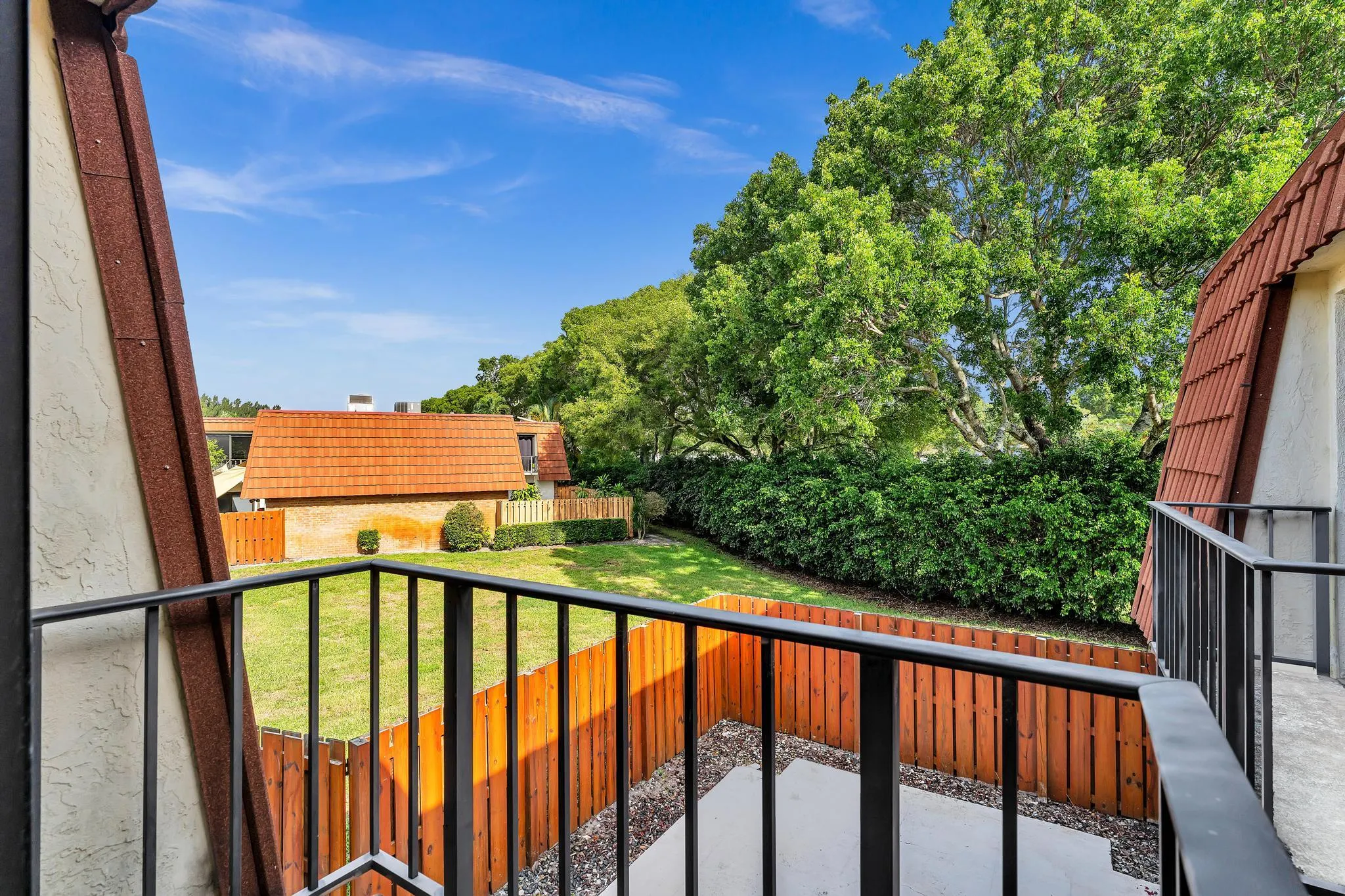 Balcony with black metal railings, overlooking a private fenced yard with a concrete patio