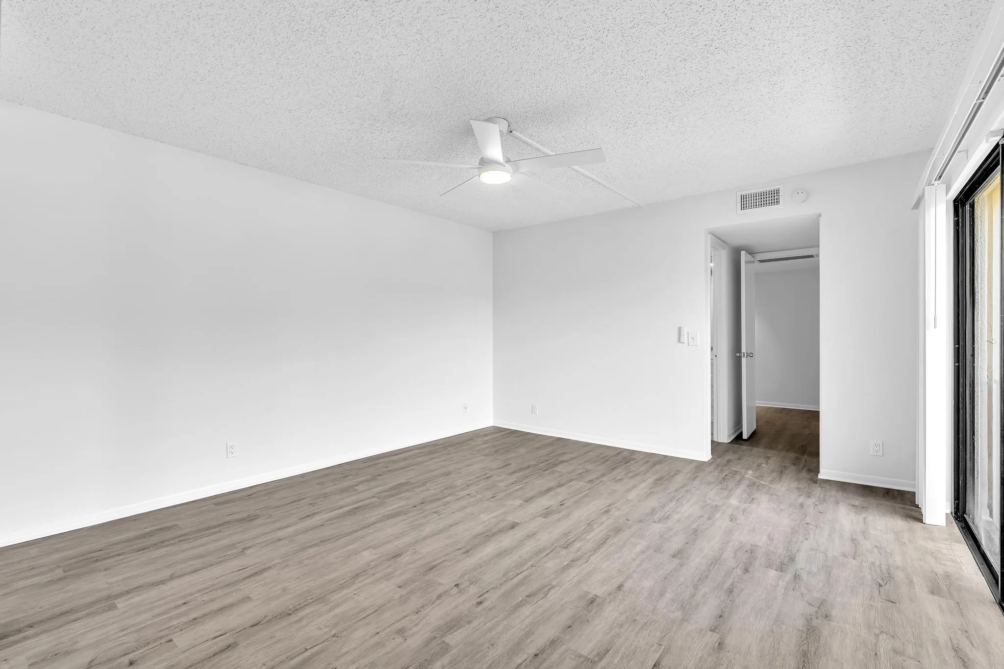 Spacious interior room featuring wood-finish flooring, a ceiling fan, and a neutral color palette
