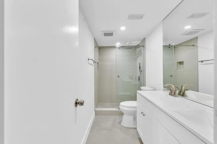 Contemporary bathroom featuring a spacious vanity with an integrated sink, a large wall-mounted mirror, and a glass-enclosed shower with a tiled niche