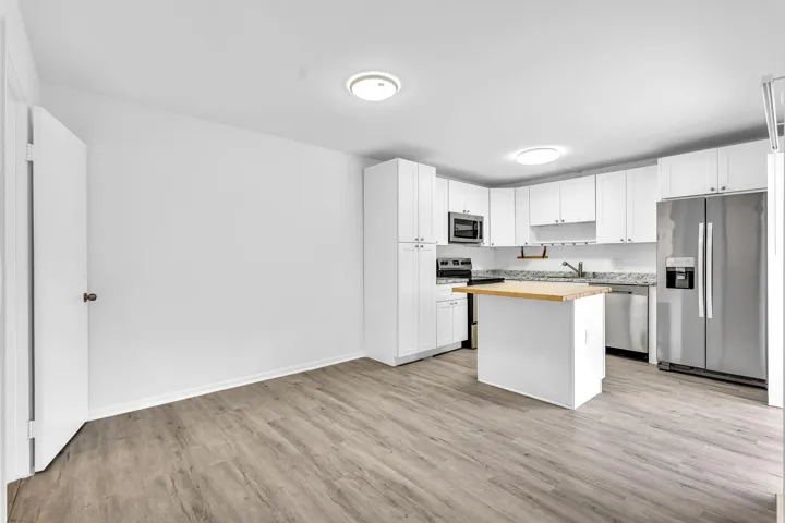 Open-concept kitchen featuring white cabinetry, gray speckled countertops, stainless steel appliances, a center island with a wood-finish top, and wood-finish flooring