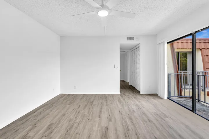 Spacious room featuring wood-finish flooring, white walls, and a ceiling fan with integrated lighting