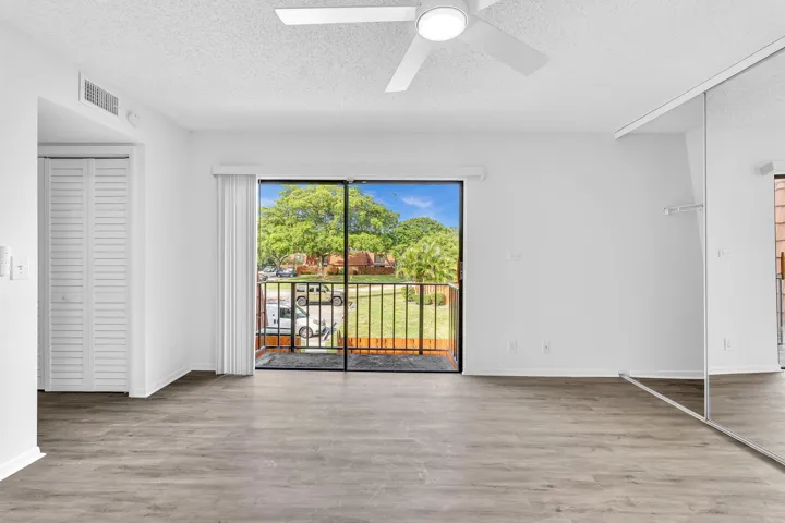 Open room featuring wood-finish flooring, a ceiling fan with integrated lighting, mirrored closet doors, and a sliding glass door to a private balcony