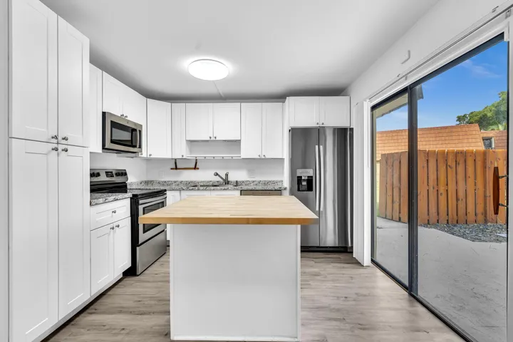 Modern kitchen featuring white shaker cabinetry, stainless steel appliances, light granite countertops, a butcher block island, and wood-finish flooring