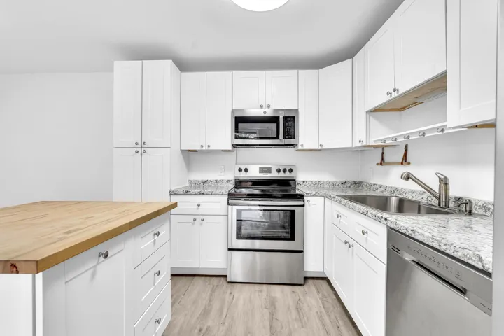 Kitchen featuring white cabinetry, stainless steel appliances, speckled countertops, and wood-finish flooring