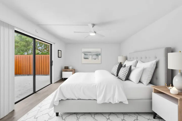 Bright bedroom featuring expansive sliding glass doors, a modern ceiling fan, light wood-finish flooring, and a private outdoor patio with a wooden privacy fence