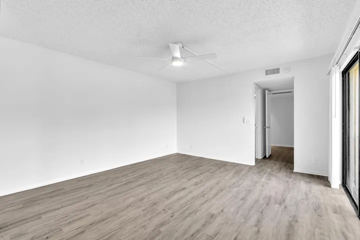 Spacious interior room featuring wood-finish flooring, a ceiling fan, and a neutral color palette