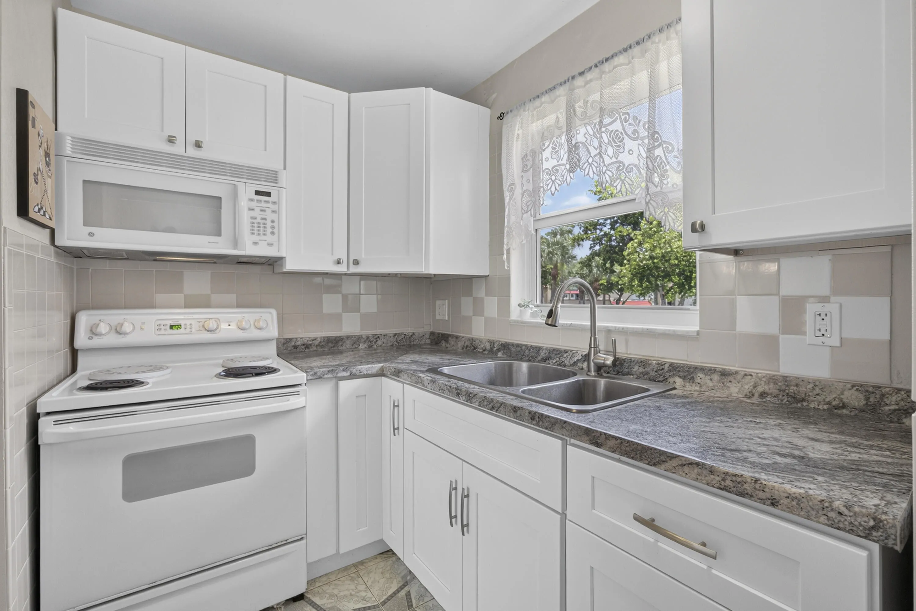 Modern kitchen featuring white cabinetry, stone-finish countertops, stainless steel double-basin sink, white over-the-range microwave, and a white electric range