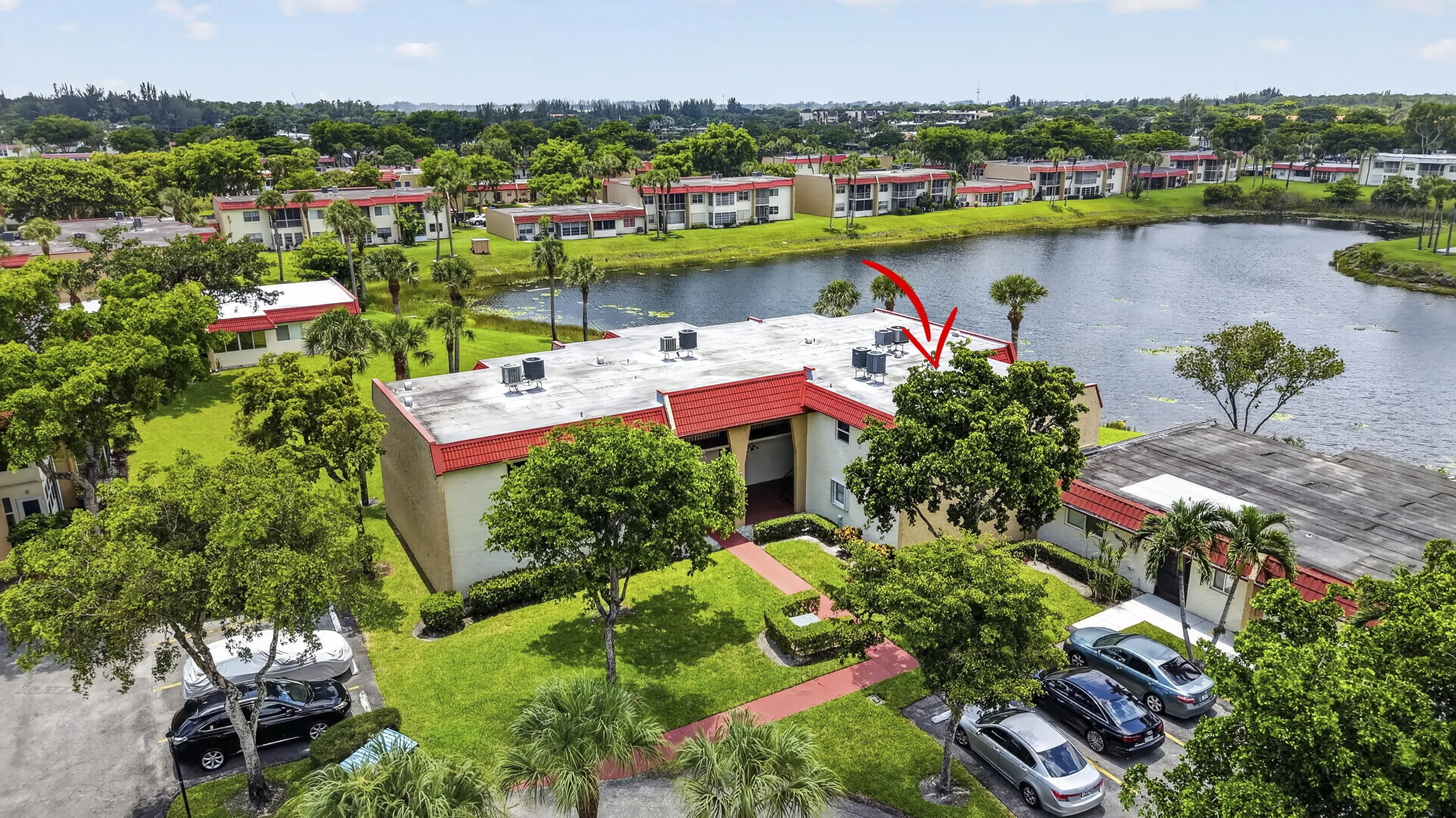 Waterfront property featuring a red tile roof, lush green landscaping, and ample surface parking