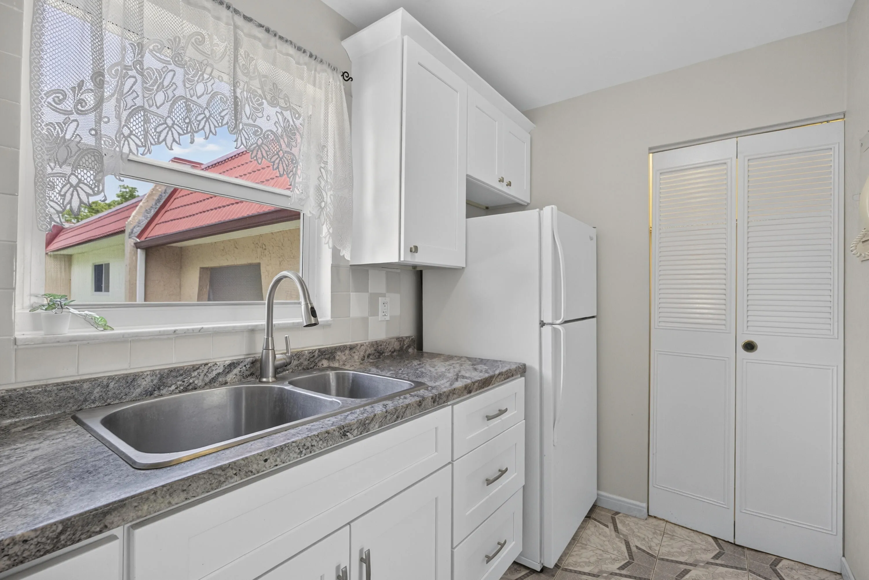 Kitchen featuring white cabinetry, a dual basin stainless steel sink with a high-arc faucet, and granite-look countertops