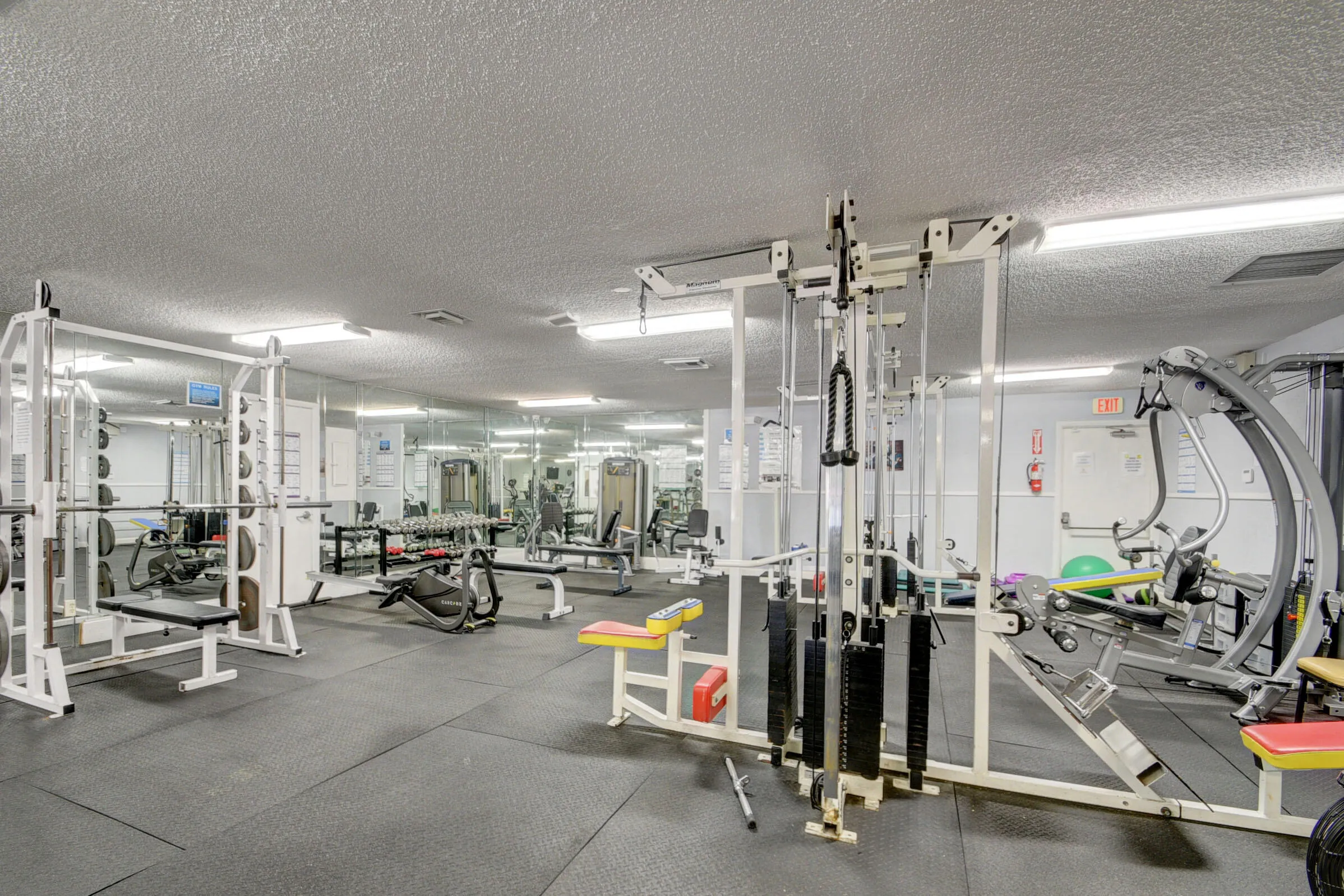 Dedicated fitness center featuring rubber flooring, mirrored walls, fluorescent lighting, and various exercise equipment including weight machines and benches