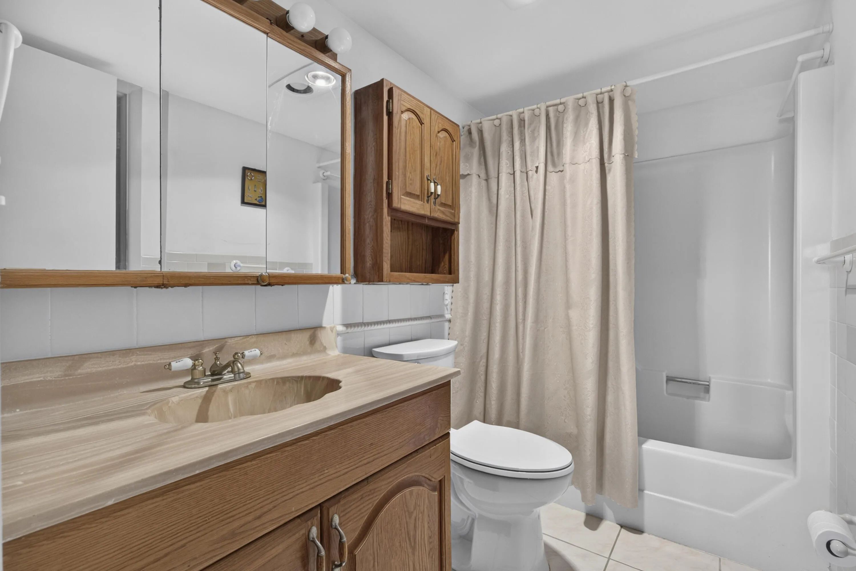 Bathroom featuring a wood-finish vanity with an integrated sink, a matching wall-mounted medicine cabinet, and a white tiled backsplash