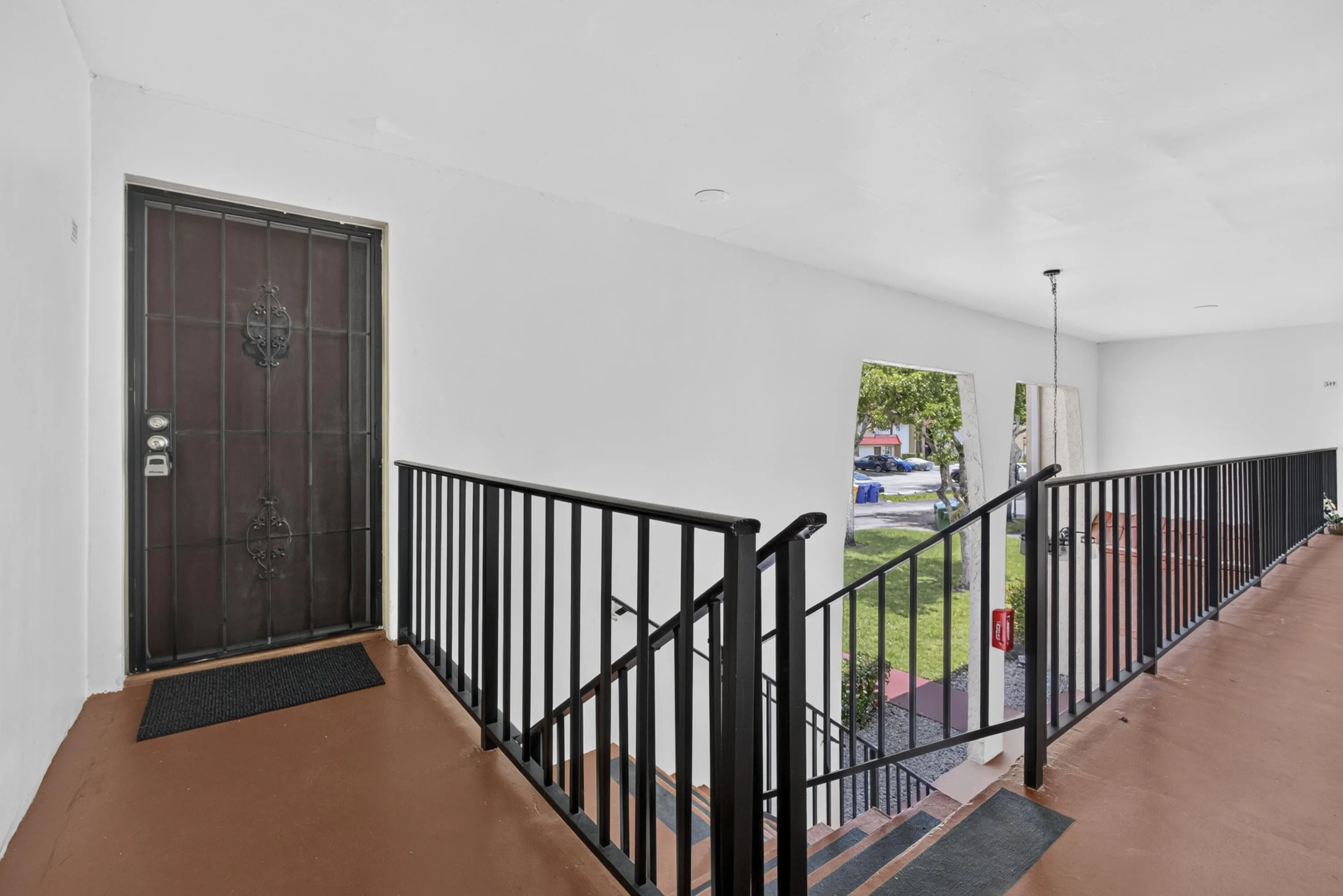 Entryway featuring a dark paneled door with decorative wrought iron security gate, white walls, and a warm-toned flooring material