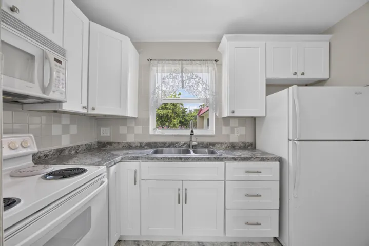 Modern kitchen featuring white cabinetry with brushed nickel hardware, a stainless steel double basin sink, and a tiled backsplash