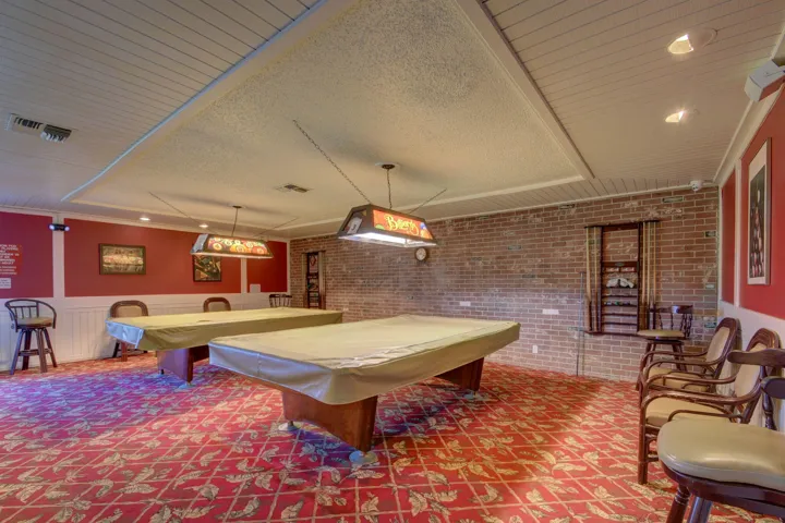 Recreation room featuring two covered billiard tables, patterned carpet, red walls with wainscoting, and an exposed brick wall accent