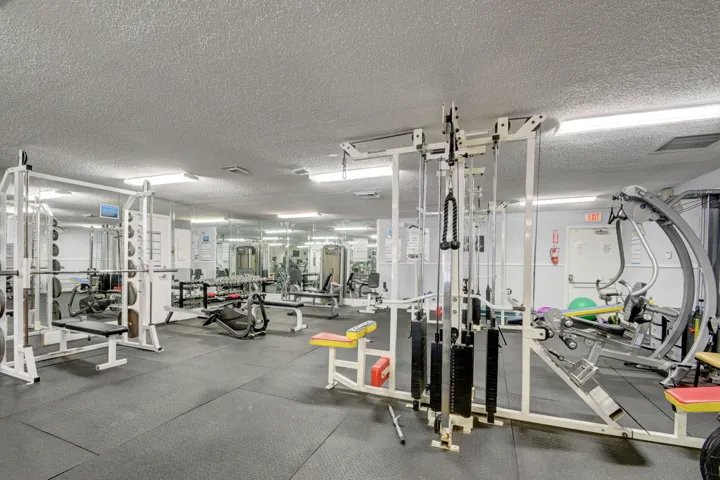 Dedicated fitness center featuring rubber flooring, mirrored walls, fluorescent lighting, and various exercise equipment including weight machines and benches