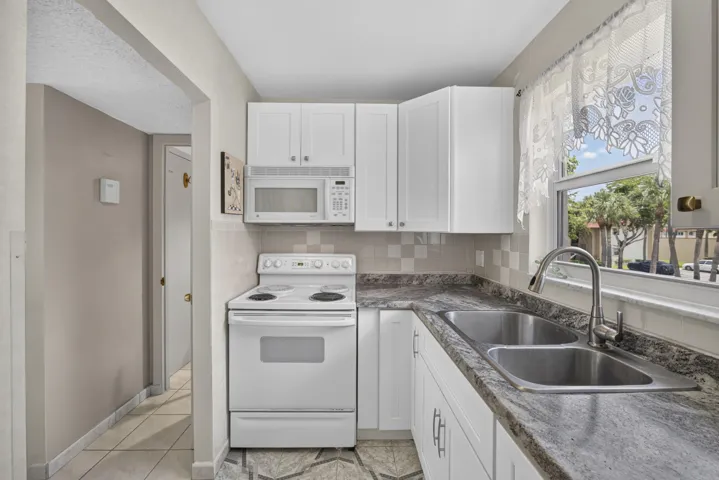 Kitchen featuring white shaker cabinetry, patterned countertop, stainless steel double basin sink with a gooseneck faucet, white electric range, and an over-the-range microwave