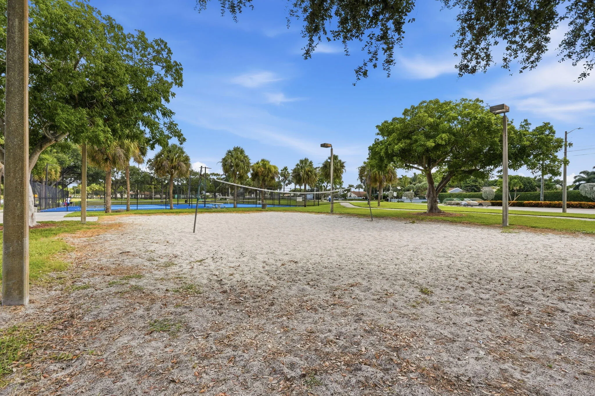 Sand volleyball court with a net, bordered by green grass and mature trees