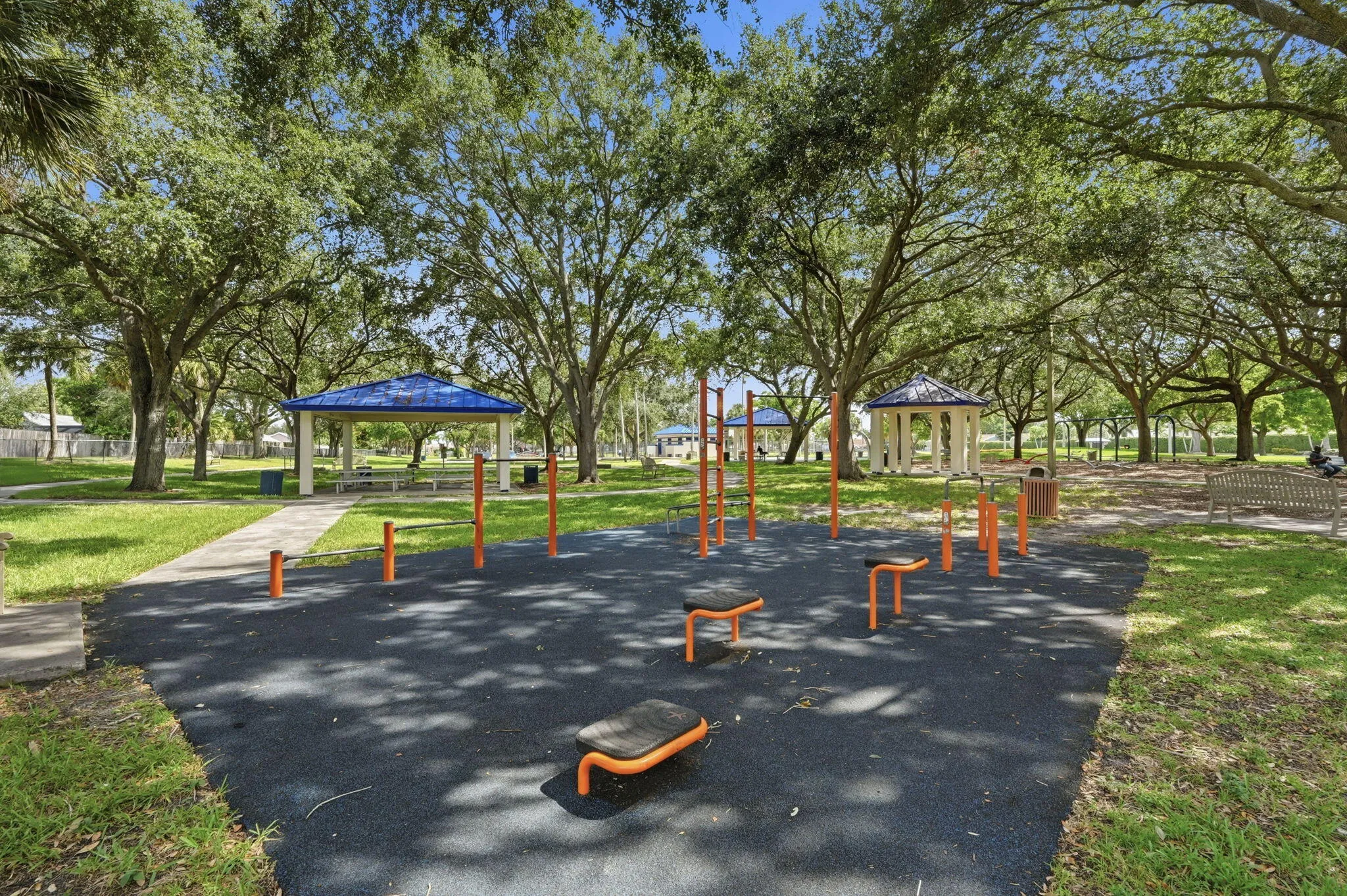 Outdoor fitness equipment on a dark, textured surface, surrounded by mature trees and manicured grass