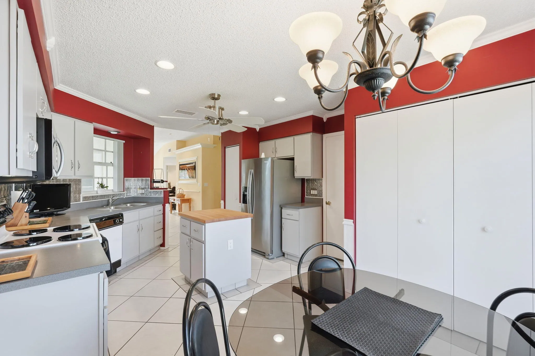 Spacious kitchen featuring white cabinetry, stainless steel appliances, a center island with butcher block countertop, and tile flooring