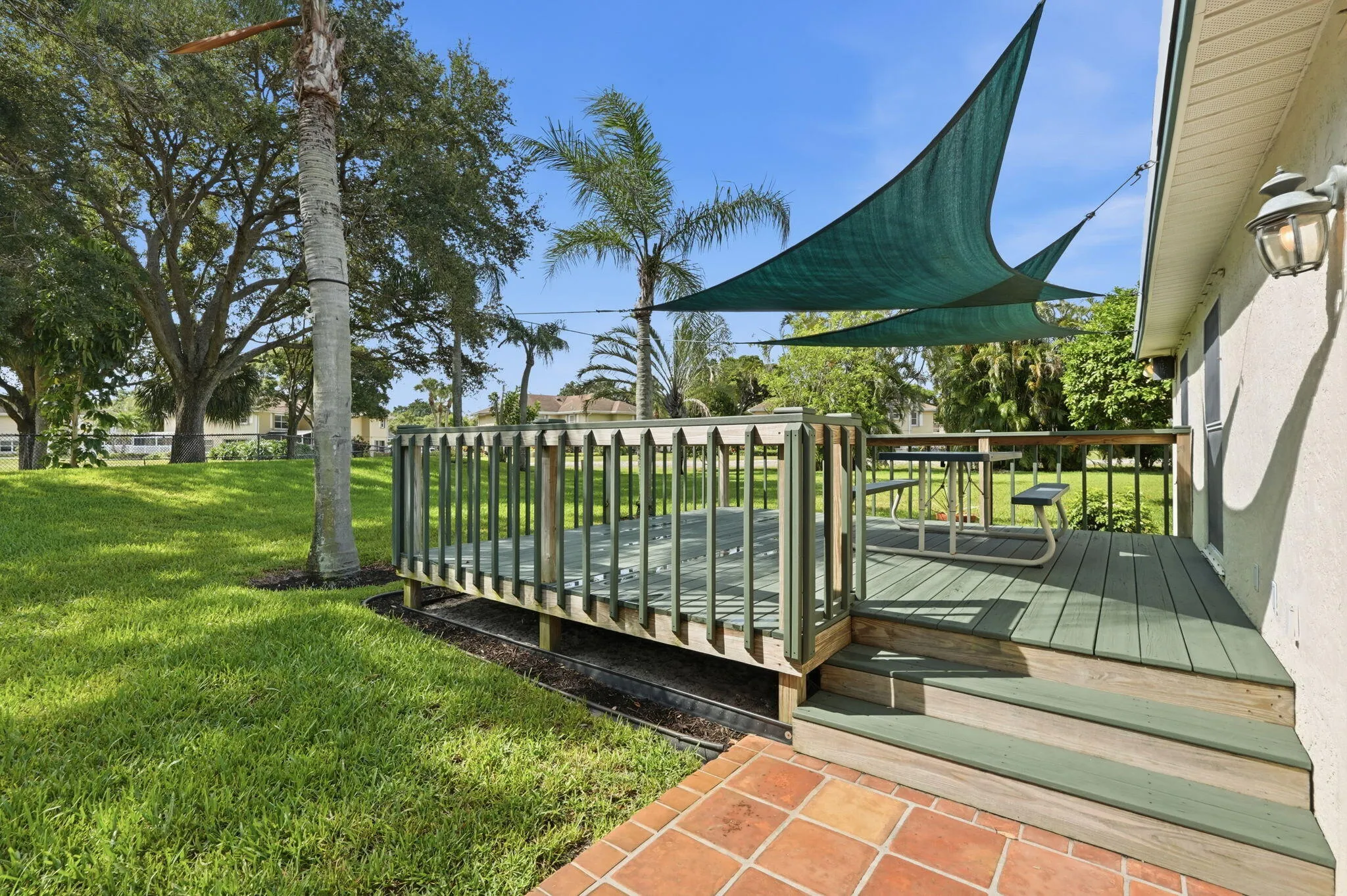 Expansive outdoor deck featuring wood-finish decking and railing, with two shade sails providing coverage