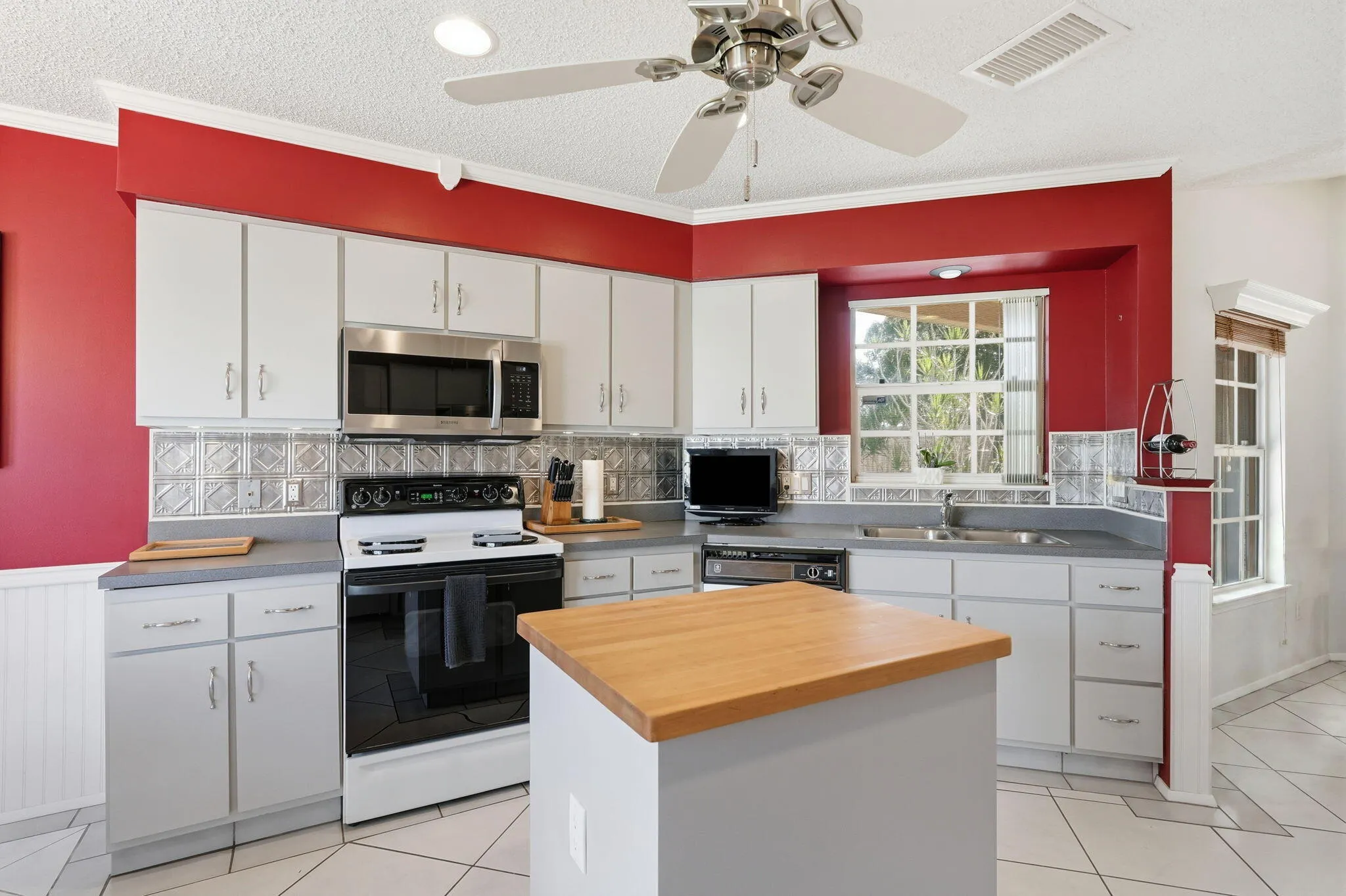 Kitchen featuring white cabinetry, grey countertops, stainless steel microwave, and a center island with a wood-finish top