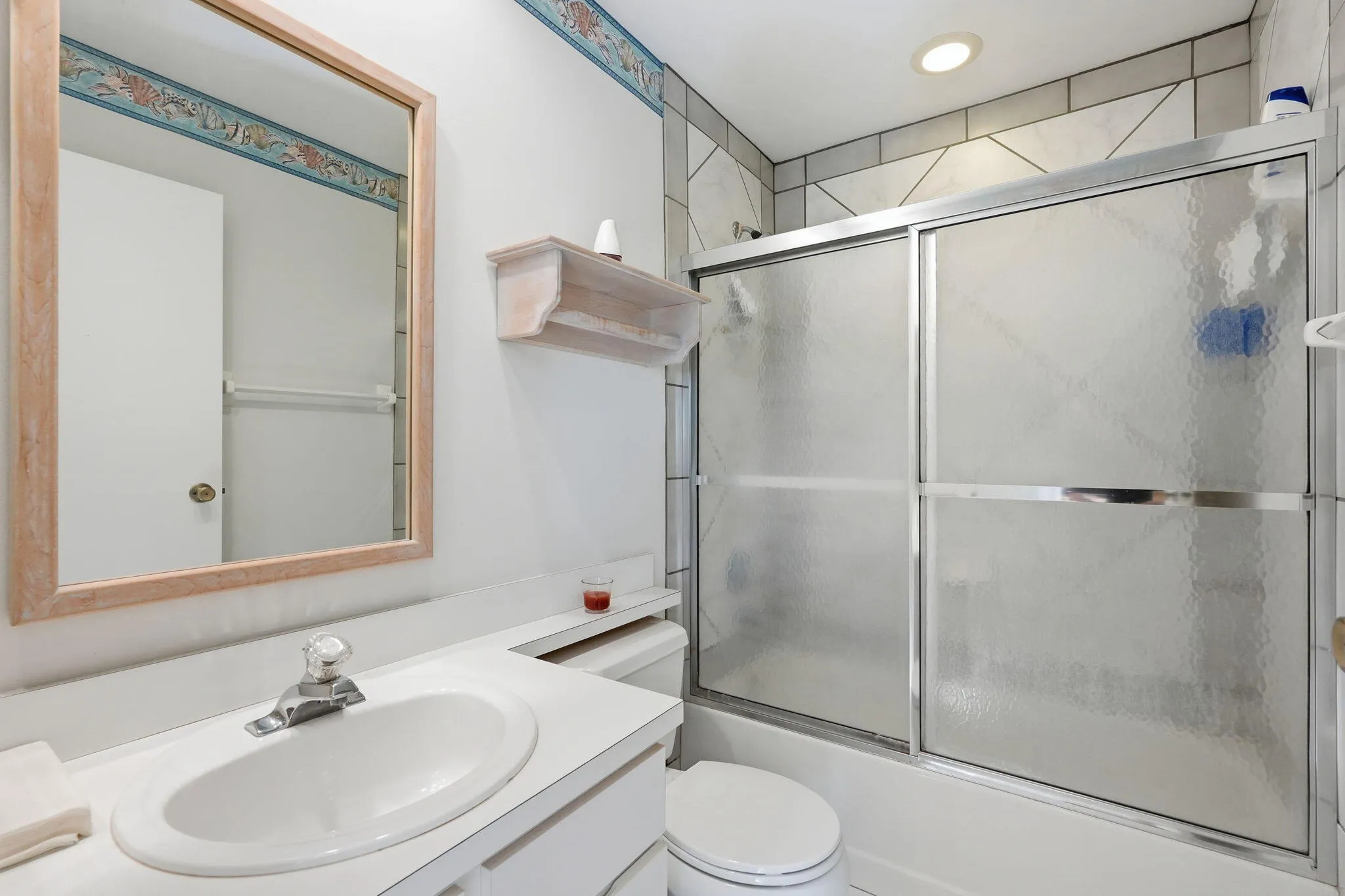 Full bathroom featuring a framed mirror, vanity with an integrated sink, and a shower-tub combination with sliding frosted glass doors