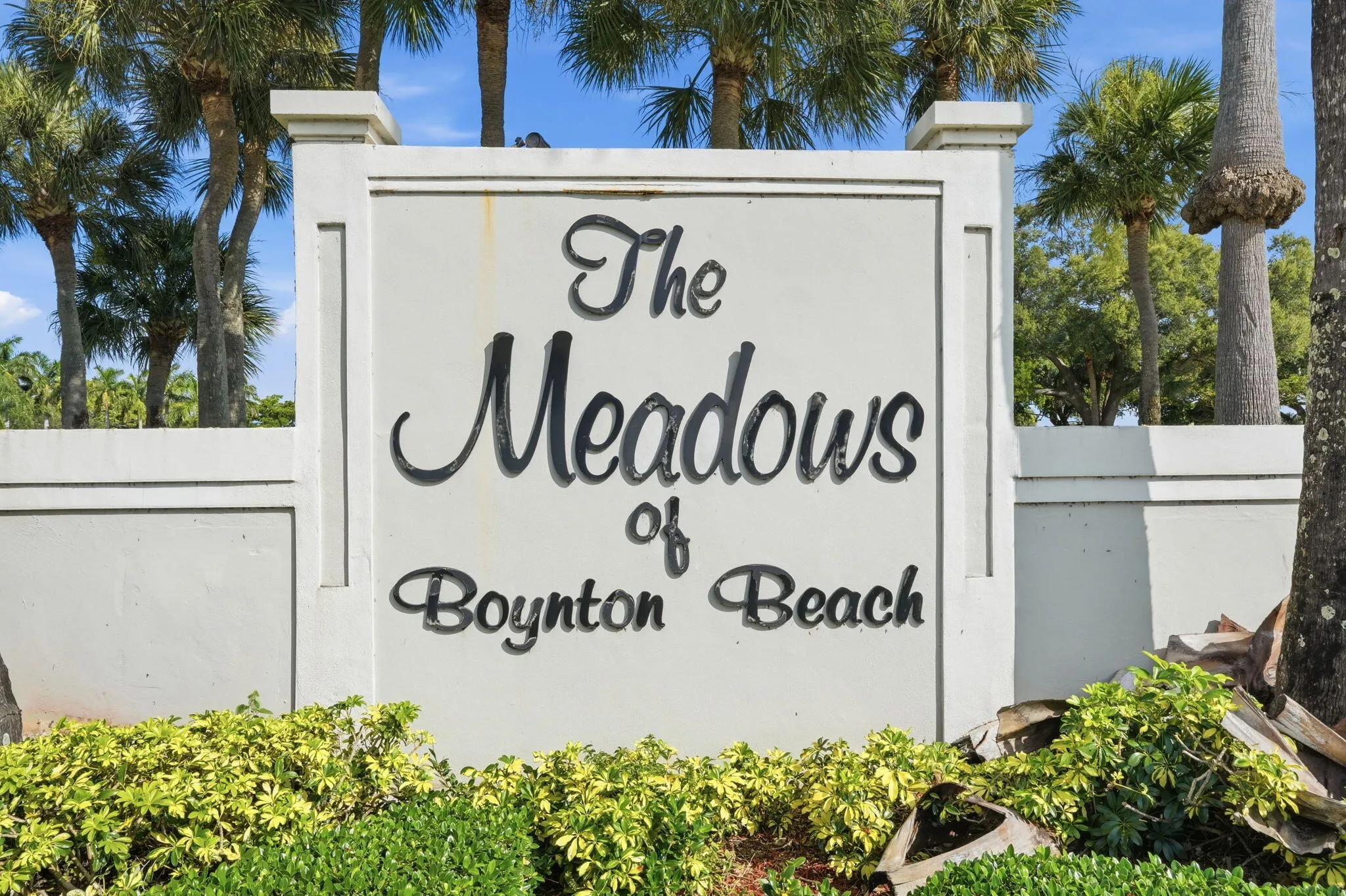 Community entrance signage featuring established palm trees and manicured ground plantings