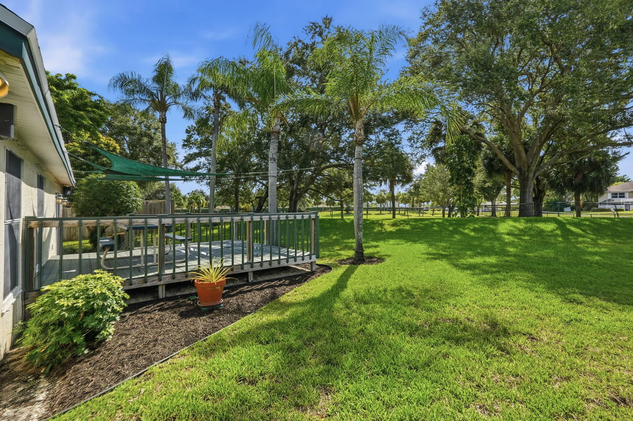 Outdoor deck featuring a wood railing and a sun shade, bordered by cultivated landscaping