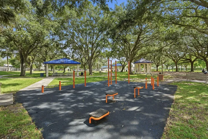 Outdoor fitness equipment on a dark, textured surface, surrounded by mature trees and manicured grass