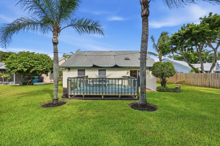 Expansive backyard featuring a wood deck with railings, mature palm trees, a well-kept lawn, and a privacy fence