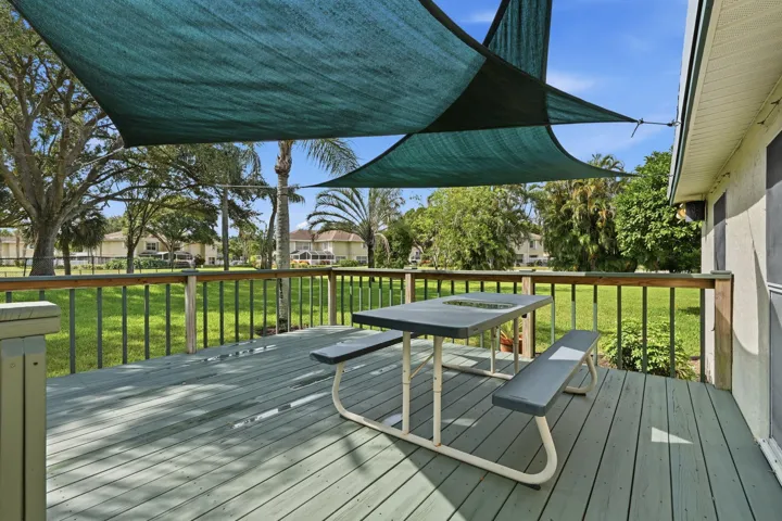 Expansive outdoor deck featuring a shade sail, wood railing, and a view of a green lawn and mature trees
