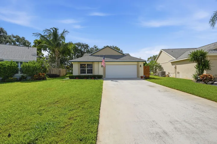 Warm beige stucco exterior with a gray shingle roof, featuring a two-car garage, a concrete driveway, and a verdant lawn