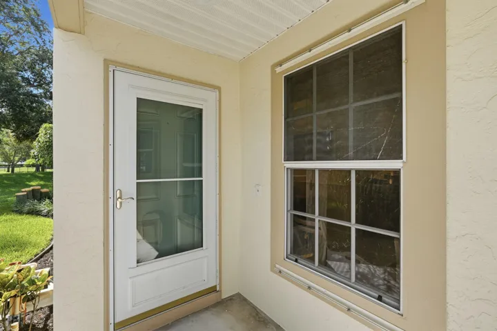 Cream stucco exterior featuring a white storm door with glass panels and a multi-pane window with a screen