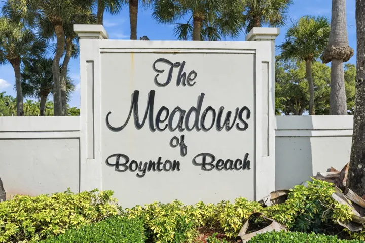 Community entrance signage featuring established palm trees and manicured ground plantings
