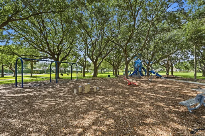 Shaded playground featuring wood chip surfacing, multiple swing sets, and a blue play structure