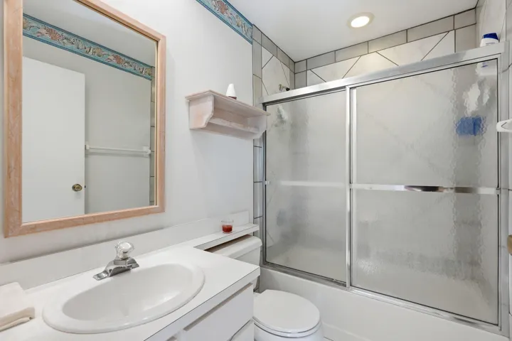 Full bathroom featuring a framed mirror, vanity with an integrated sink, and a shower-tub combination with sliding frosted glass doors