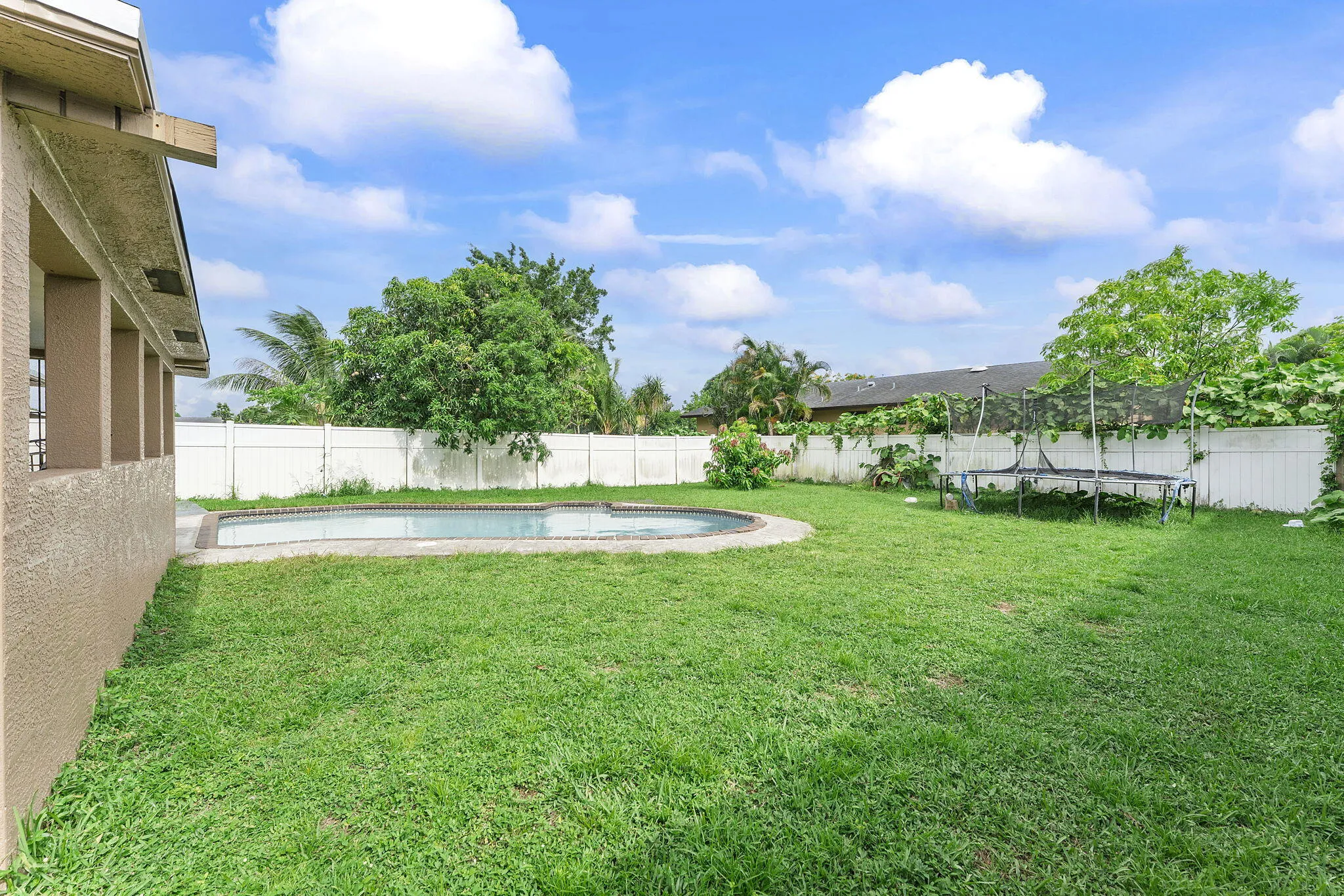 Expansive backyard featuring a kidney-shaped in-ground pool, perimeter fencing, and mature trees