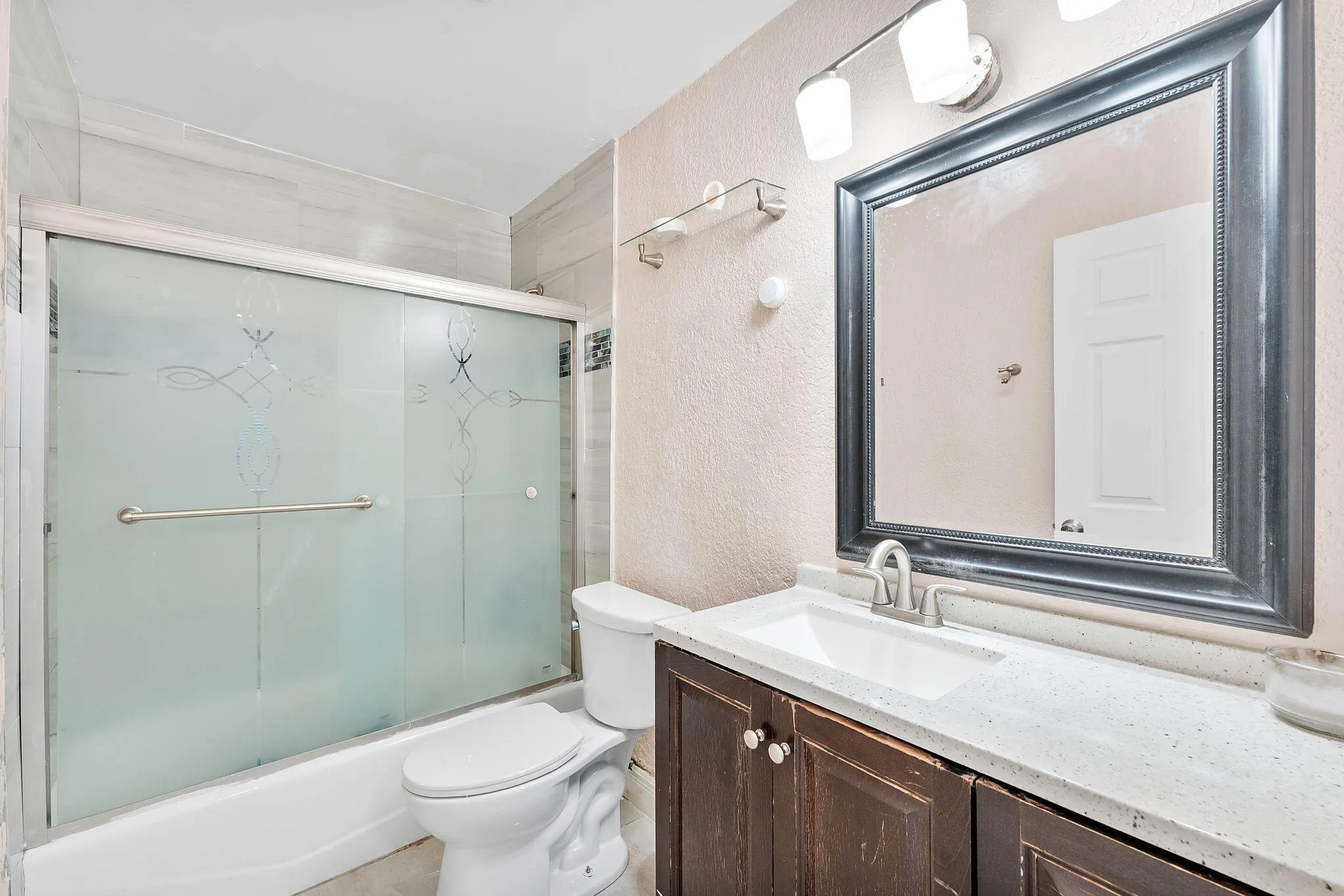 Bathroom featuring a tub with frosted sliding glass doors, a vanity with wood-finish cabinetry, a white countertop, and an undermount sink