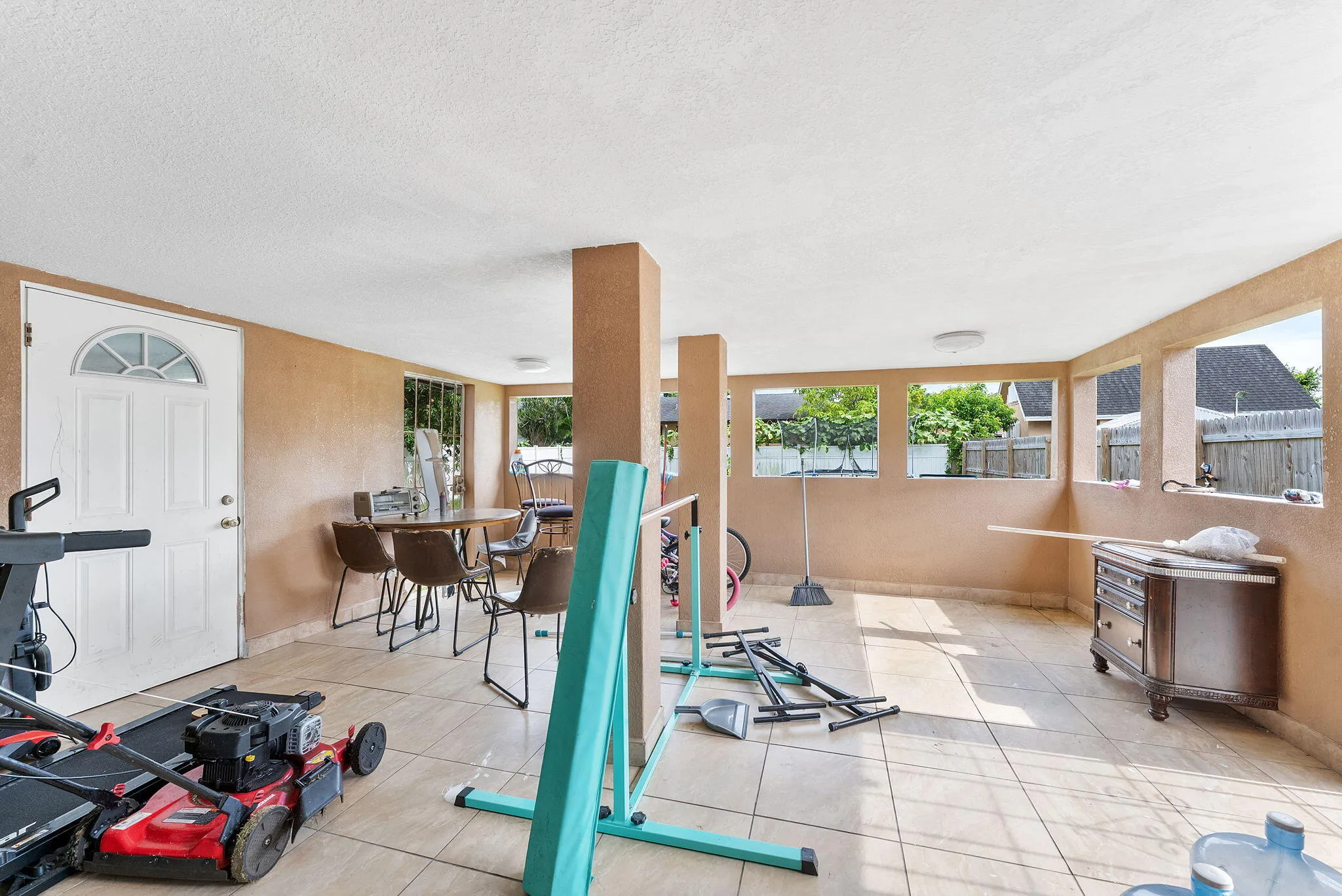 Spacious enclosed patio featuring tile flooring, multiple open wall sections, and a white entry door with an arched window insert