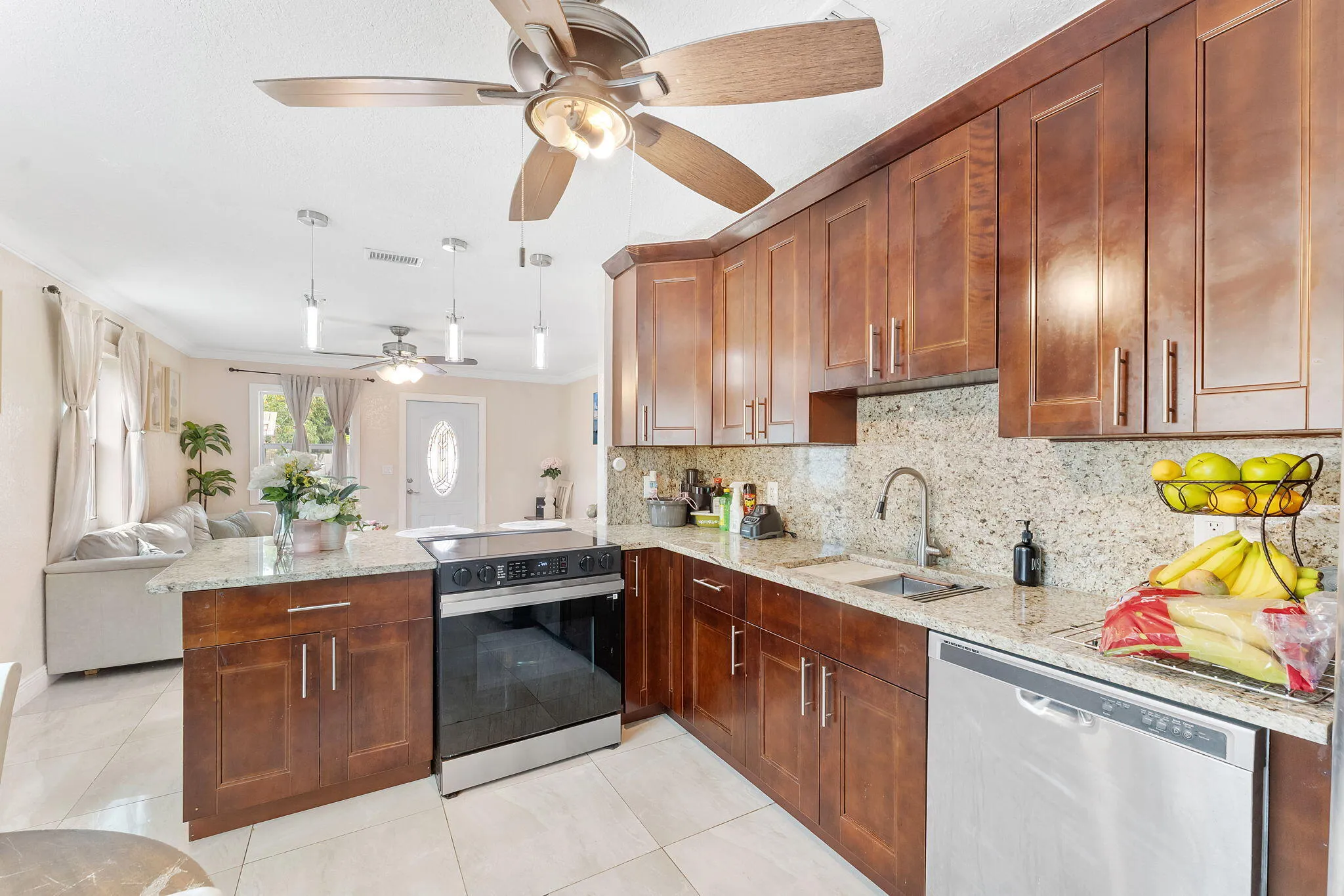 Modern kitchen featuring wood cabinetry, light-toned countertops, tile flooring, stainless steel appliances, and a central island with an integrated range