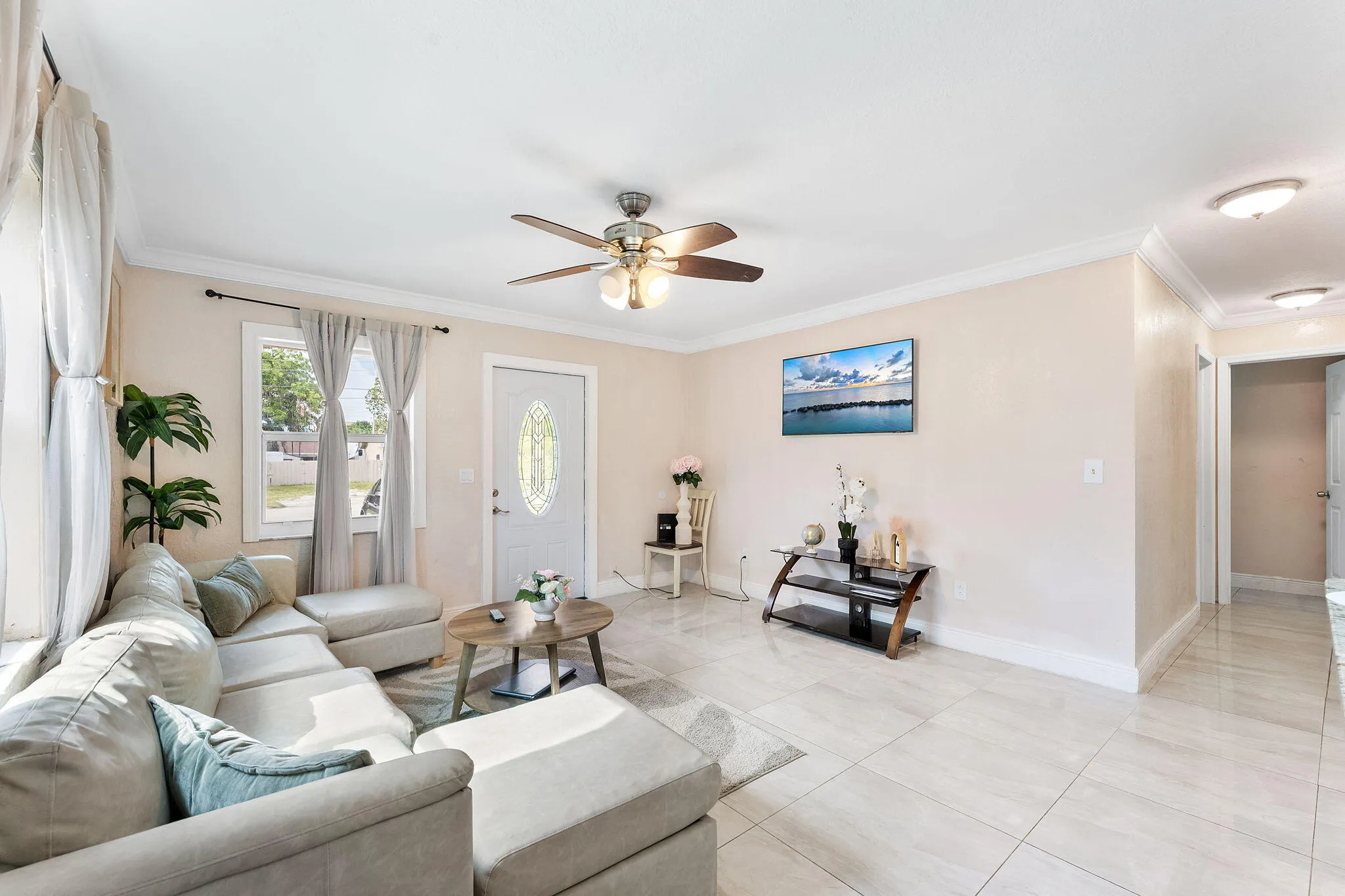 Spacious living area featuring light-toned walls, crown molding, and large format tile flooring