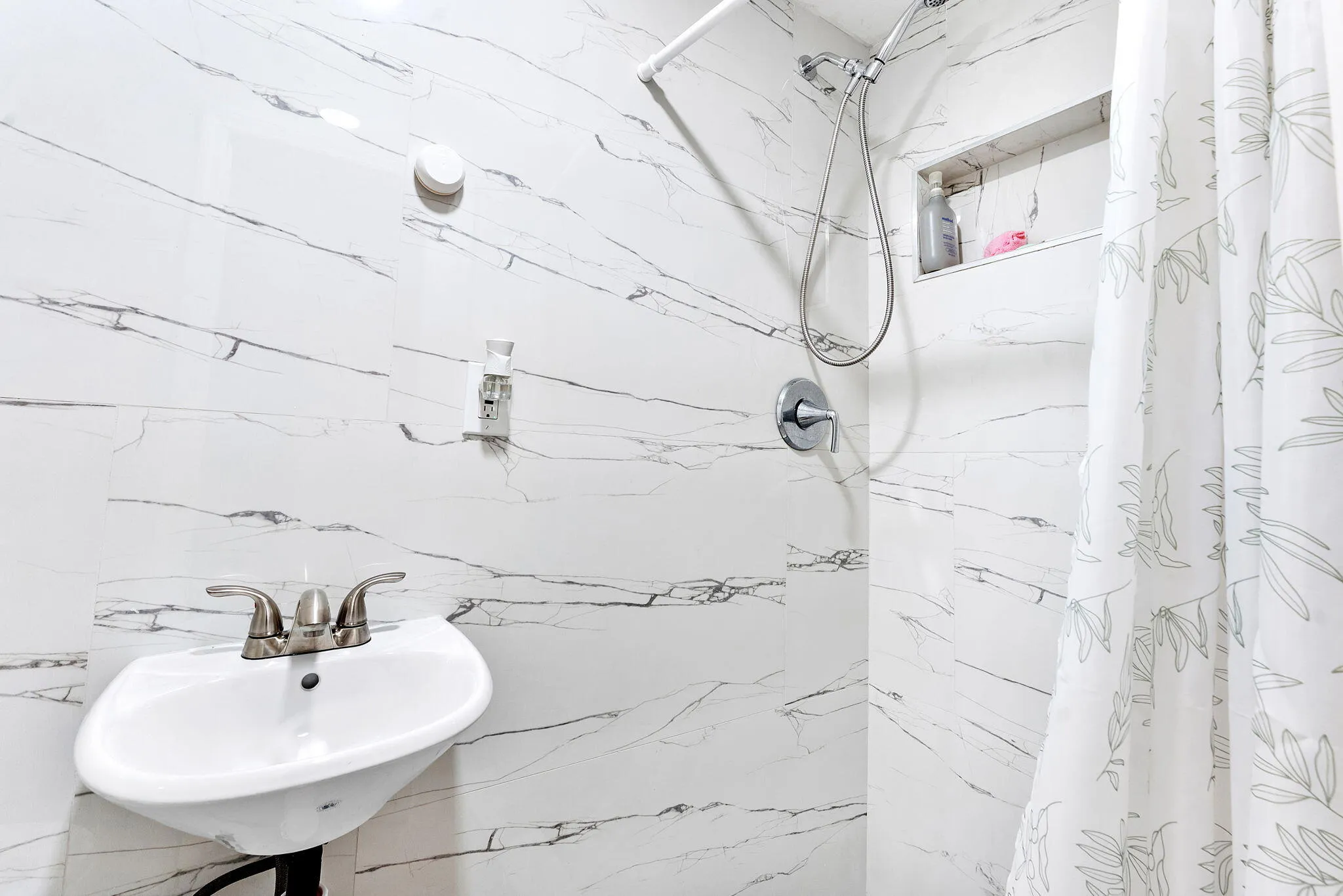 White tiled shower with a built-in niche, chrome shower fixtures, and an adjacent wall-mounted sink with brushed nickel faucet