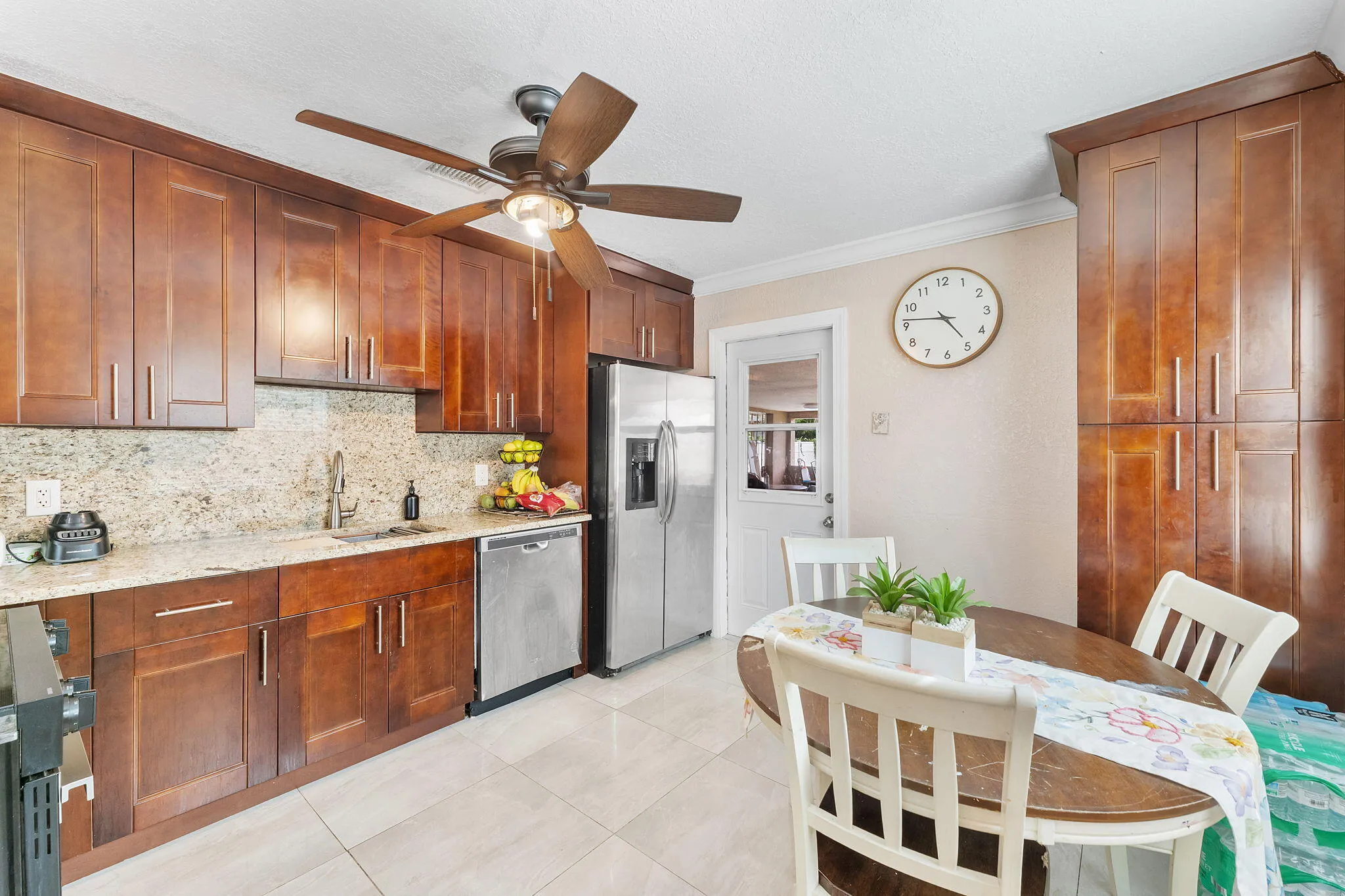 Kitchen featuring extensive wood cabinetry, granite countertops, tile flooring, stainless steel appliances, and a ceiling fan with integrated lighting