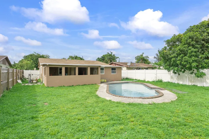 Backyard featuring a concrete deck swimming pool, enclosed patio with screens, and a manicured lawn