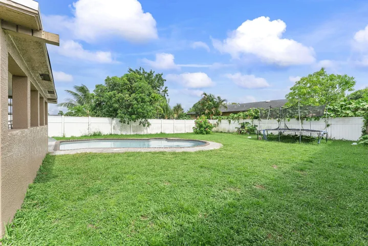 Expansive backyard featuring a kidney-shaped in-ground pool, perimeter fencing, and mature trees